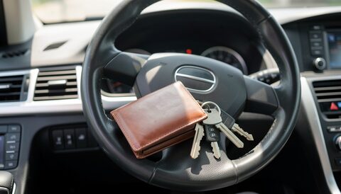 Leather wallet and a set of keys resting on the steering wheel of a parked car in daylight